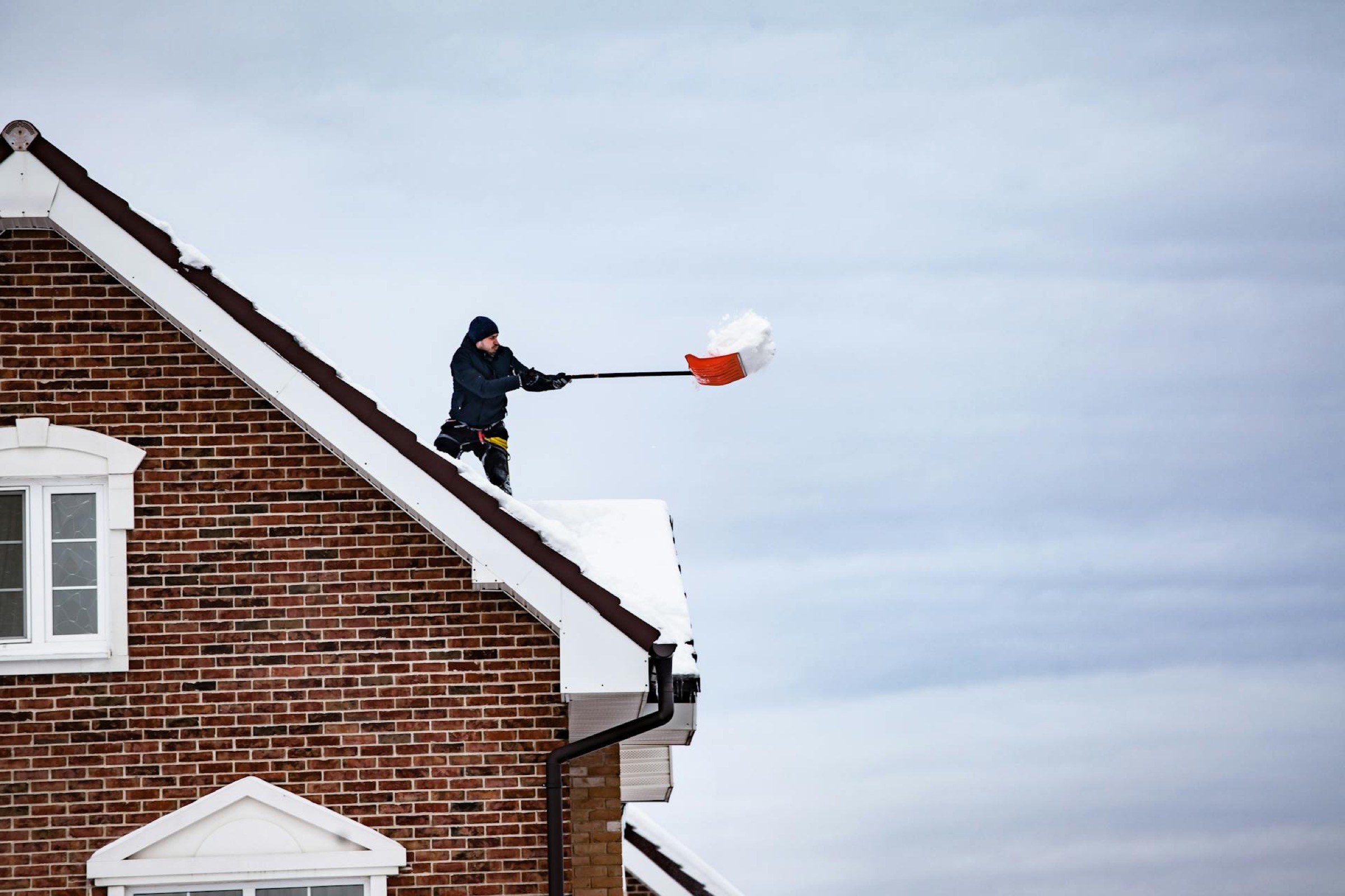Arbetslag skottar snö från ett villatak för hand med snöskyffel
