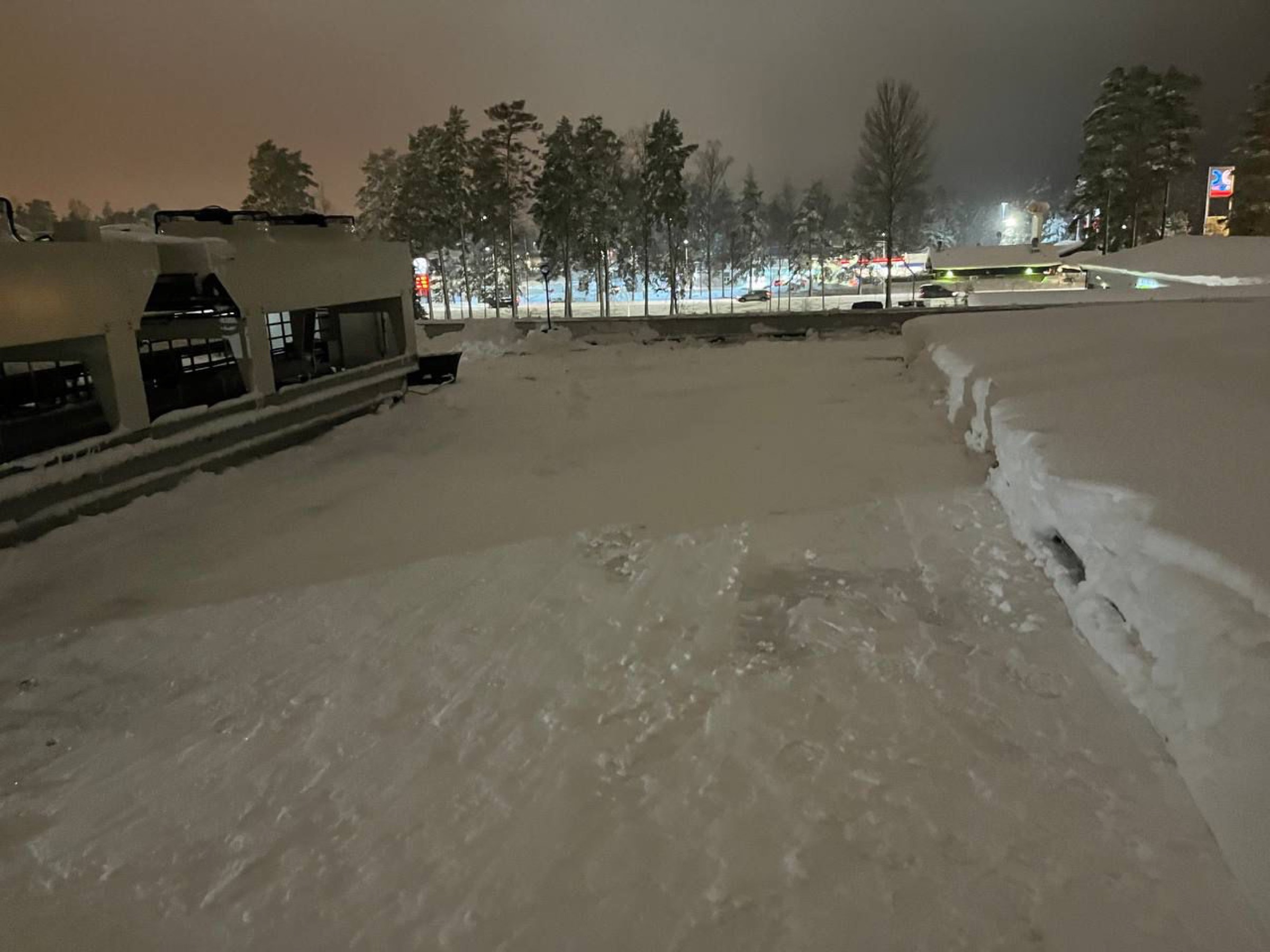 Snöröjning av tak nattetid där Arbetslag skjuter undan snön från takkanten