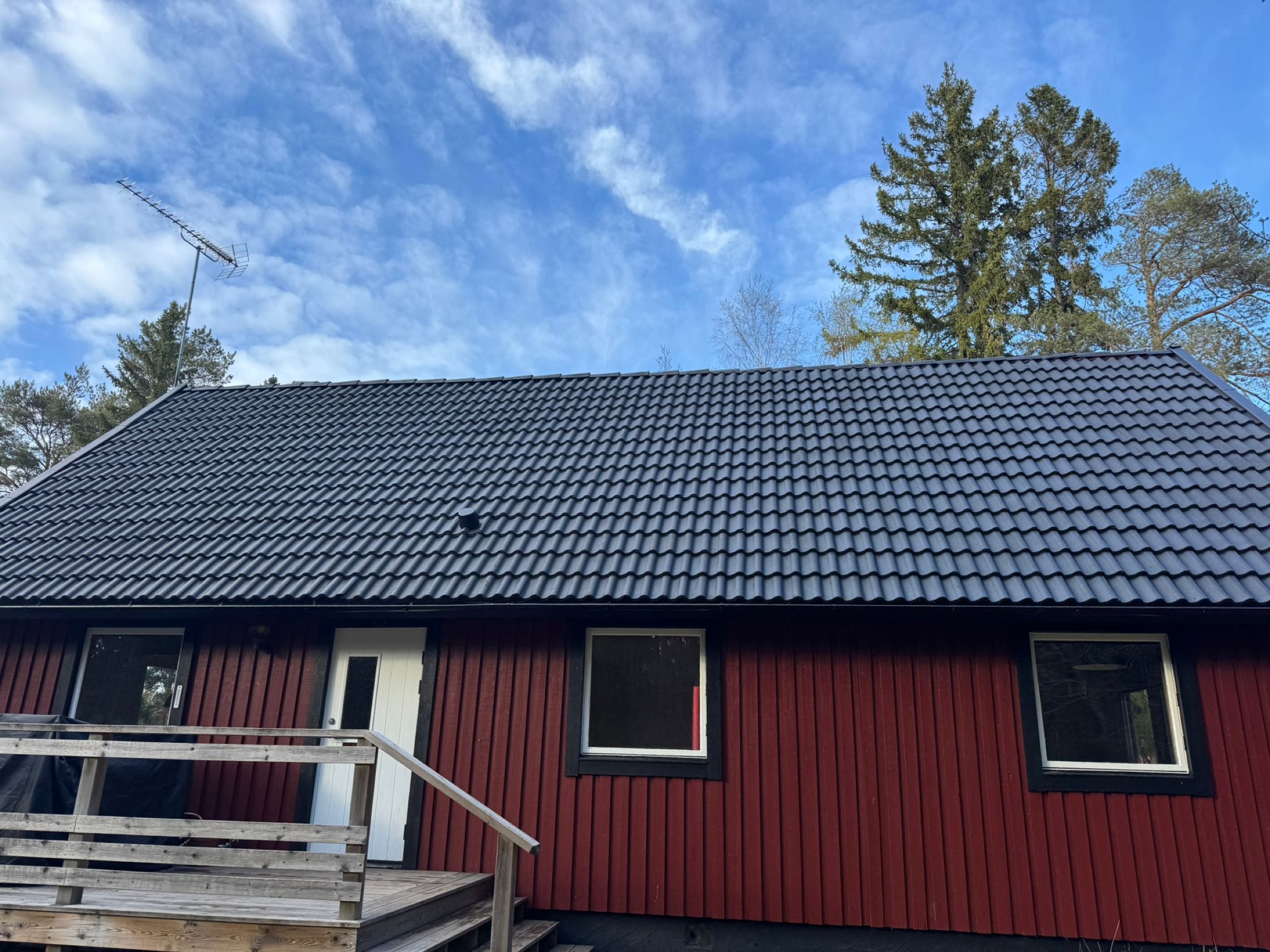 Villatak i mörk kulör mot blå himmel, underhållet av Arbetslag Bygg